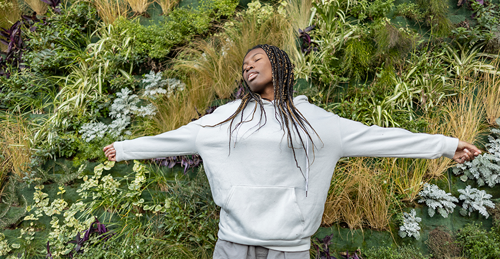 African american woman standing with arms spread in front of a vertical garden