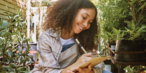 Happy woman writing on a clipboard next to plants in a garden